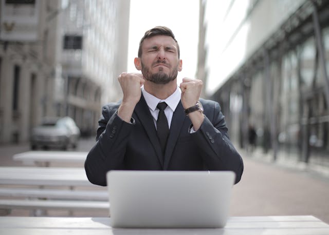 man clenching his fists in front of a laptop